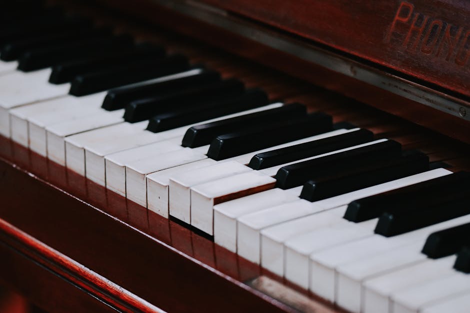 Close-up photograph of a piano keyboard, highlighting the black and white keys arranged in alternating pattern. The piano's wooden casing has a polished, reddish-brown finish, with some visible text on the upper right corner of the image. The keys are clean and well-maintained, with a slight reflection on their surface, indicating good lighting conditions. This image is taken from a slight angle, providing a detailed view of the keys extending from the foreground to the background, capturing part of the inside property where the piano might be prepared for a home relocation. The context suggests a setting focused on moving items such as furniture during a packing and moving process, consistent with professional removals services like those offered by Pimlico Movers, especially for bulky items like pianos during house removals or furniture transport.
