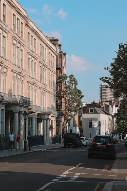 The image shows a row of narrow residential buildings lining a cobblestone street in Pimlico, SW1V, with various potted plants and small trees placed along the pavement in front of the properties. The