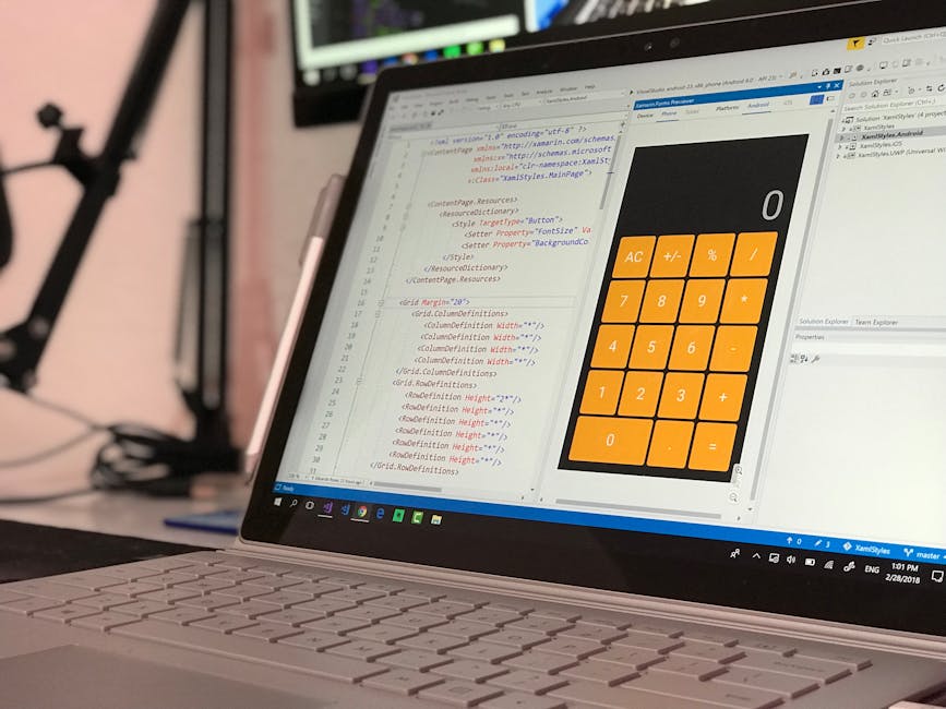 Close-up view of a laptop on a desk displaying a coding editor with HTML and CSS code on the left side and a calculator interface on the right side; the laptop is positioned inside a room with a blurr